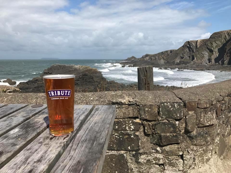 A pint of tribute with a view of the sea behind on one of the outdoor tables at the Wreckers Retreat Bar