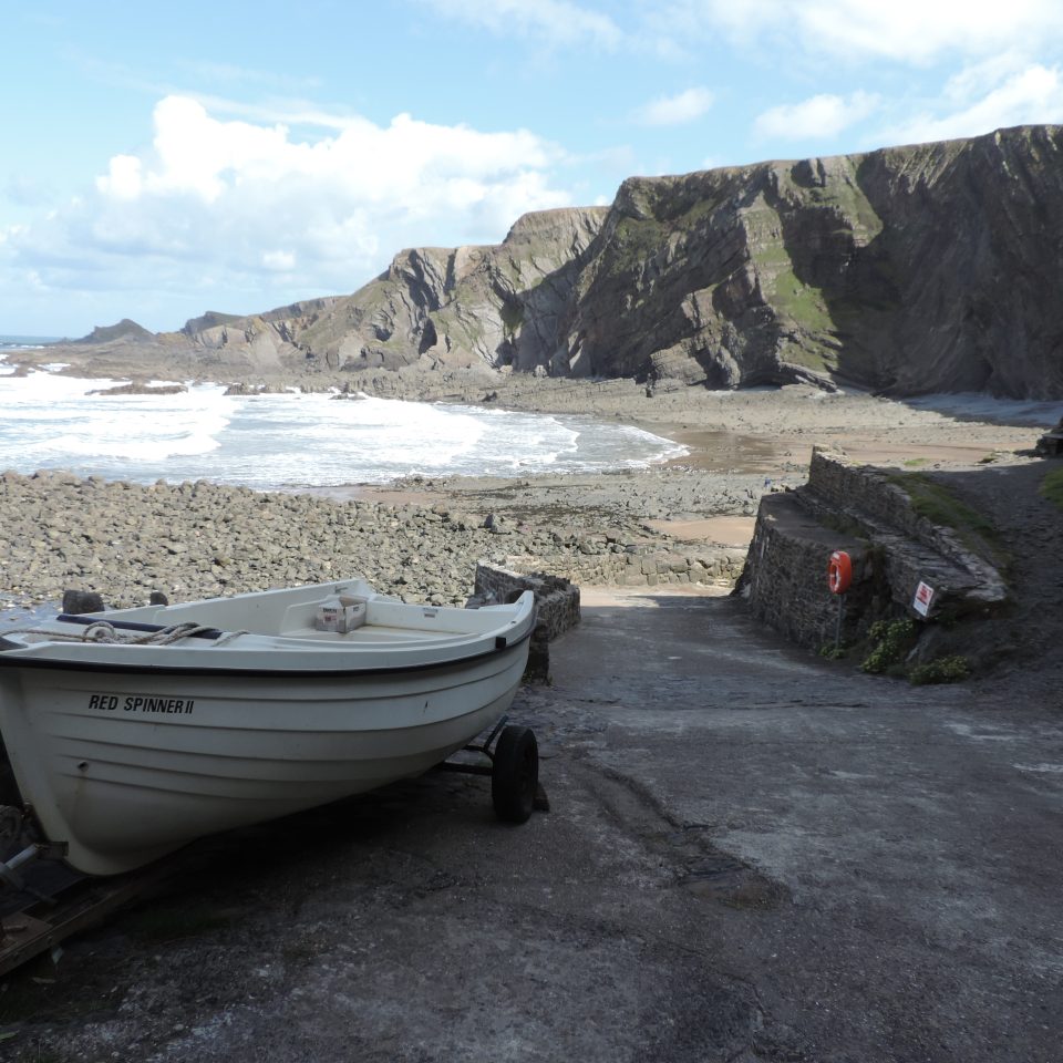 Waves breaking on shore of Hartland Quay with small docked boat in foreground