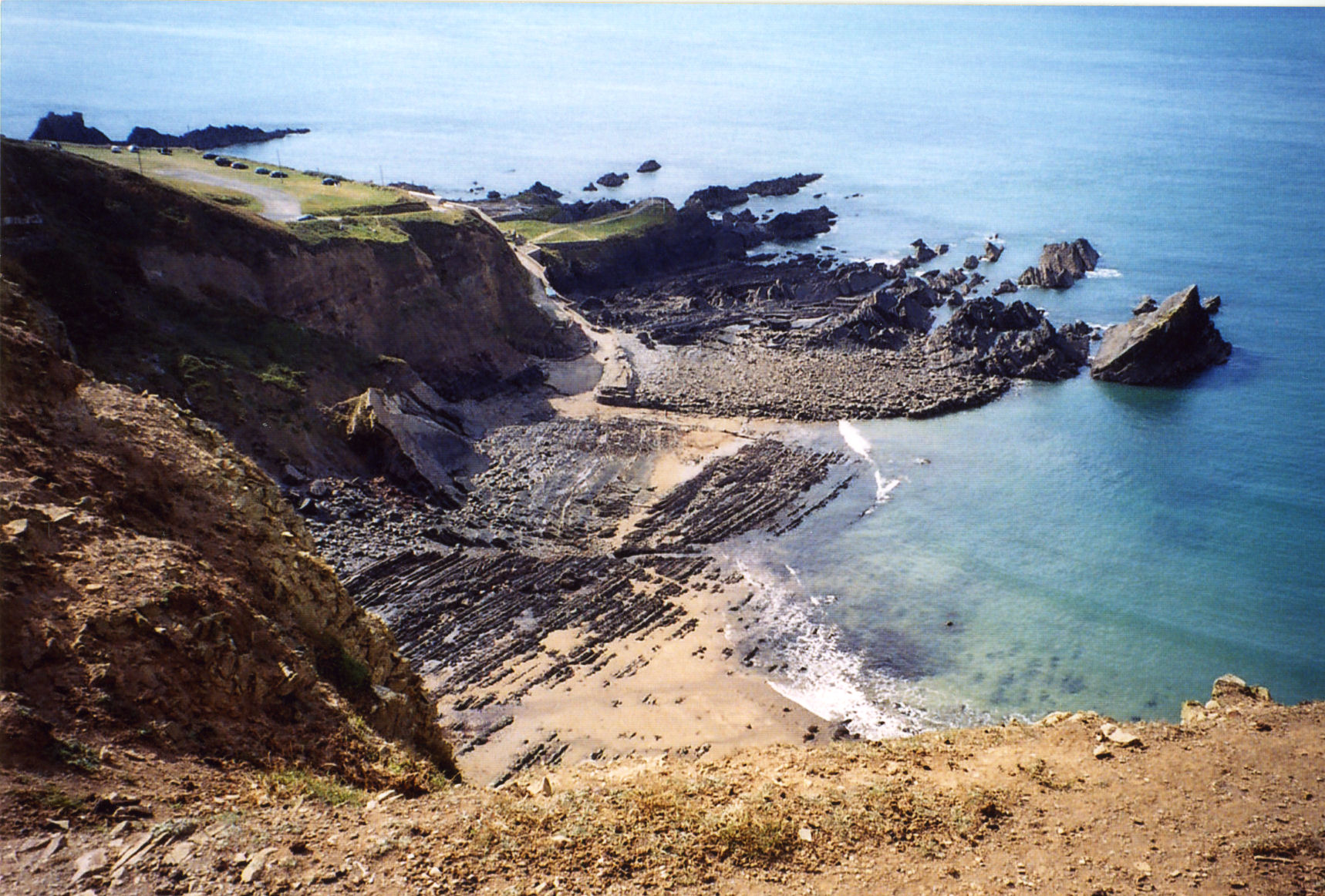 Rugged shoreline and beach at Hartland Quay with crystal clear blue waters